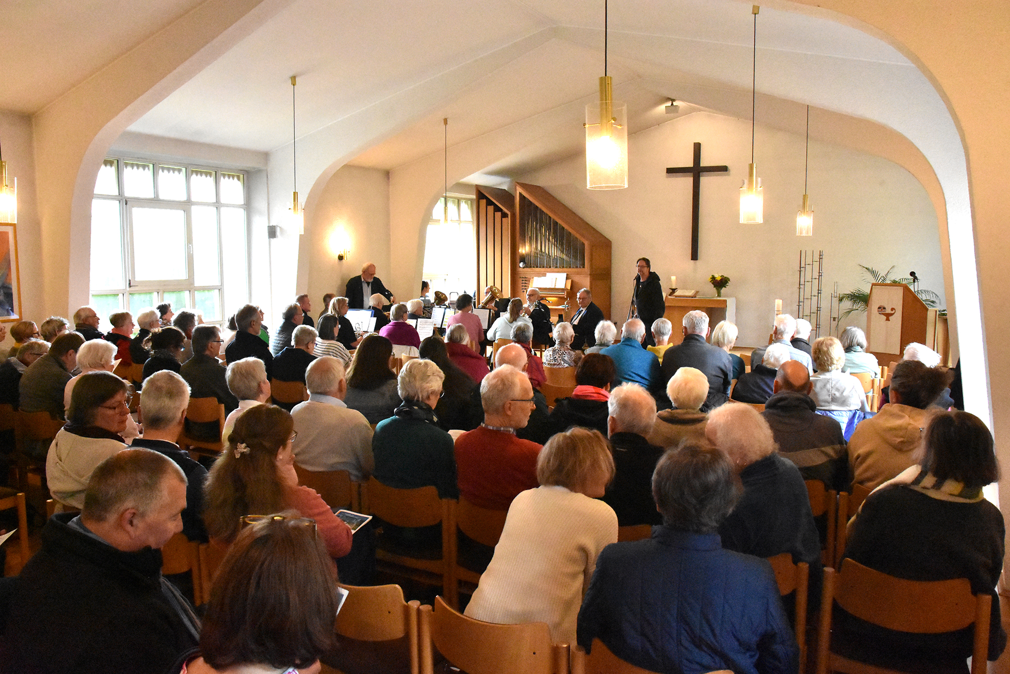 Gemeinde sitzt in einer Kirche mit sichtbarem Kreuz und Orgel während eines Gottesdienstes