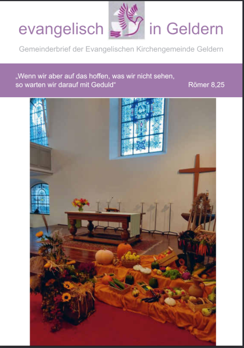 Innenraum einer Kirche mit Altar, Kreuz, buntem Erntedank-Gesteck aus Kürbissen, Sonnenblumen und anderem Gemüse vor einem Fenster mit buntem Glasfenster